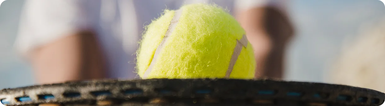 close-up of a tennis ball resting on a racket strings with shallow depth of field, highlighting texture, precision, and professional tennis equipment detail